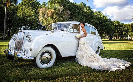 A bride leaning on the hood of her car.