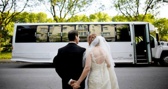 A bride and groom holding hands in front of a bus.