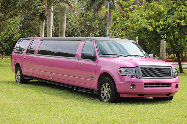 A pink limo is parked in the grass.